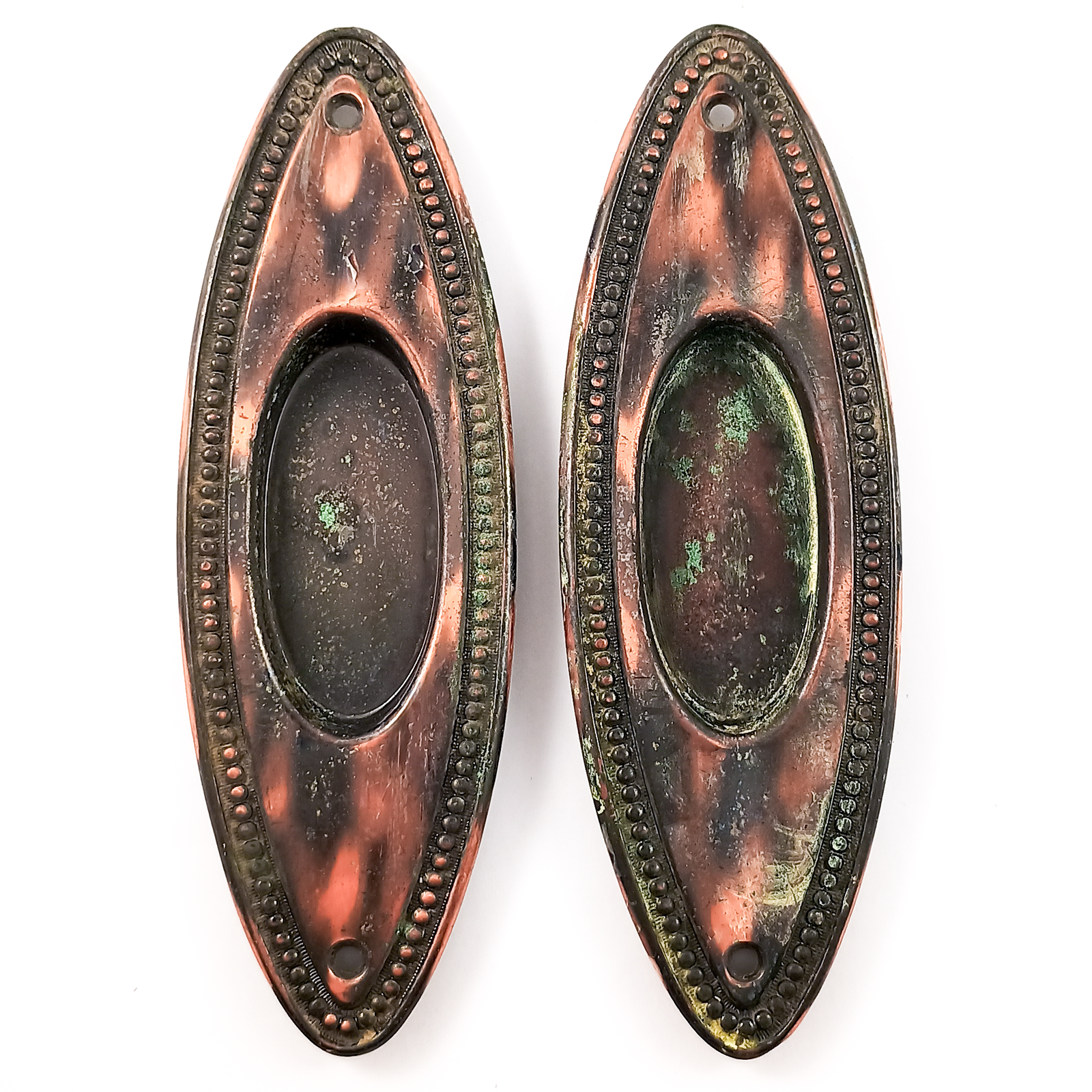 Four oval pocket door pulls with beaded trim and a copper-and-black japanned finish. One has quite a bit of verdigris along the edge, the other three have only very small amounts of verdigris. All four have keyholes.