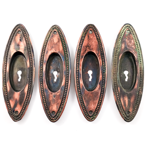 Four oval pocket door pulls with beaded trim and a copper-and-black japanned finish. One has quite a bit of verdigris along the edge, the other three have only very small amounts of verdigris. All four have keyholes.