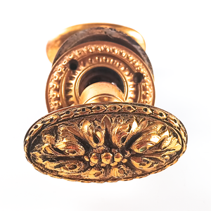 A close-up photo of one knob, showing the design more clearly - a central set of small bumps is surrounded by eight petals, and there is a somewhat geometric design around the edge of the knob. This knob shows moderate patina, especially between the petals.