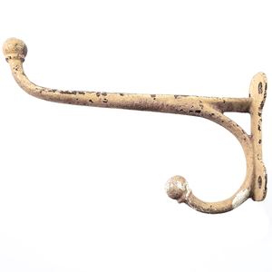 A very large cast iron coat hook facing to the left, covered in a coating of off-white paint that has worn and flaked off in spots
