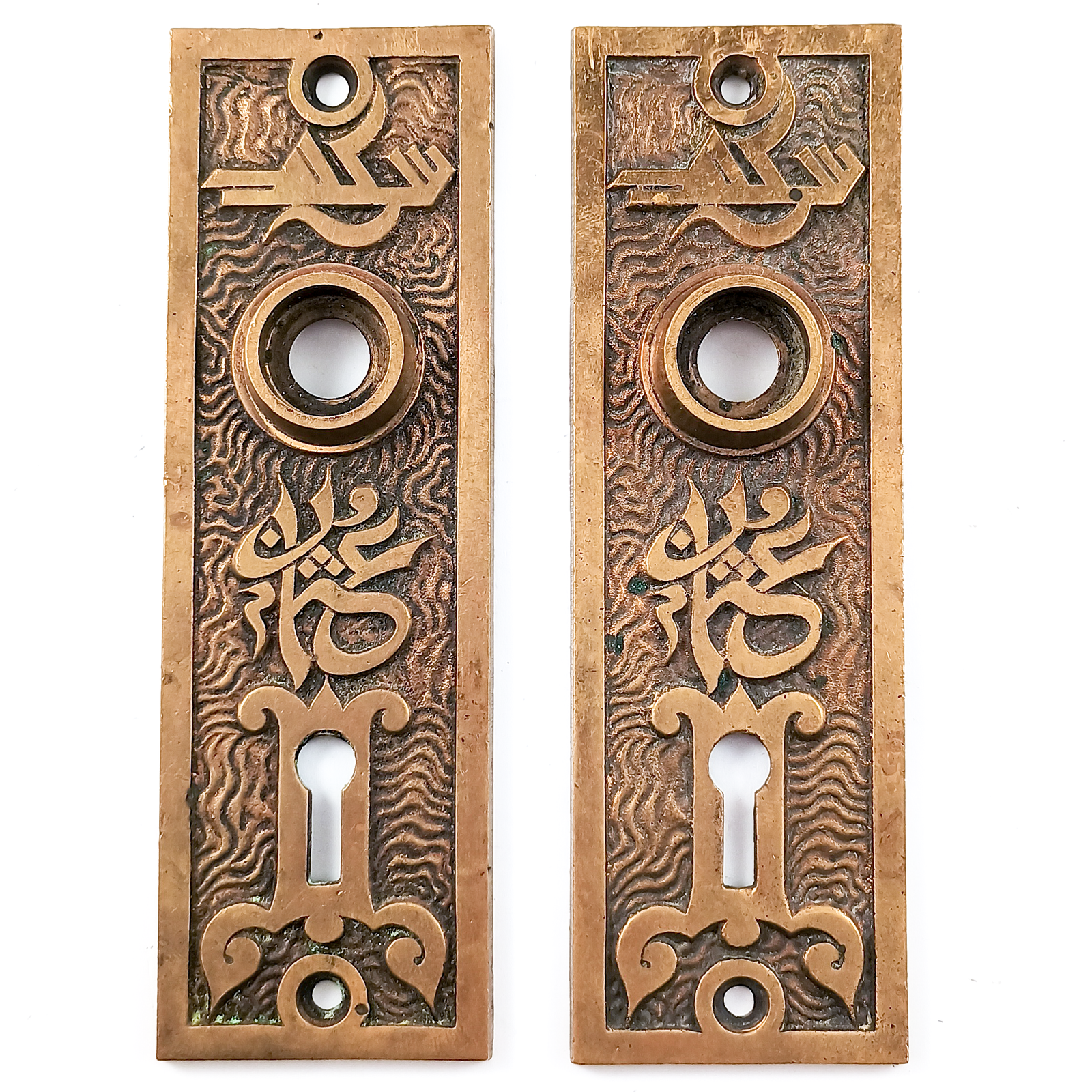 Two bronze escutcheons, each with a keyhole and a hole for a doorknob. Both escutcheons are decorated with a wavy pattern, on top of which are designs that somewhat resemble Arabic lettering and motifs