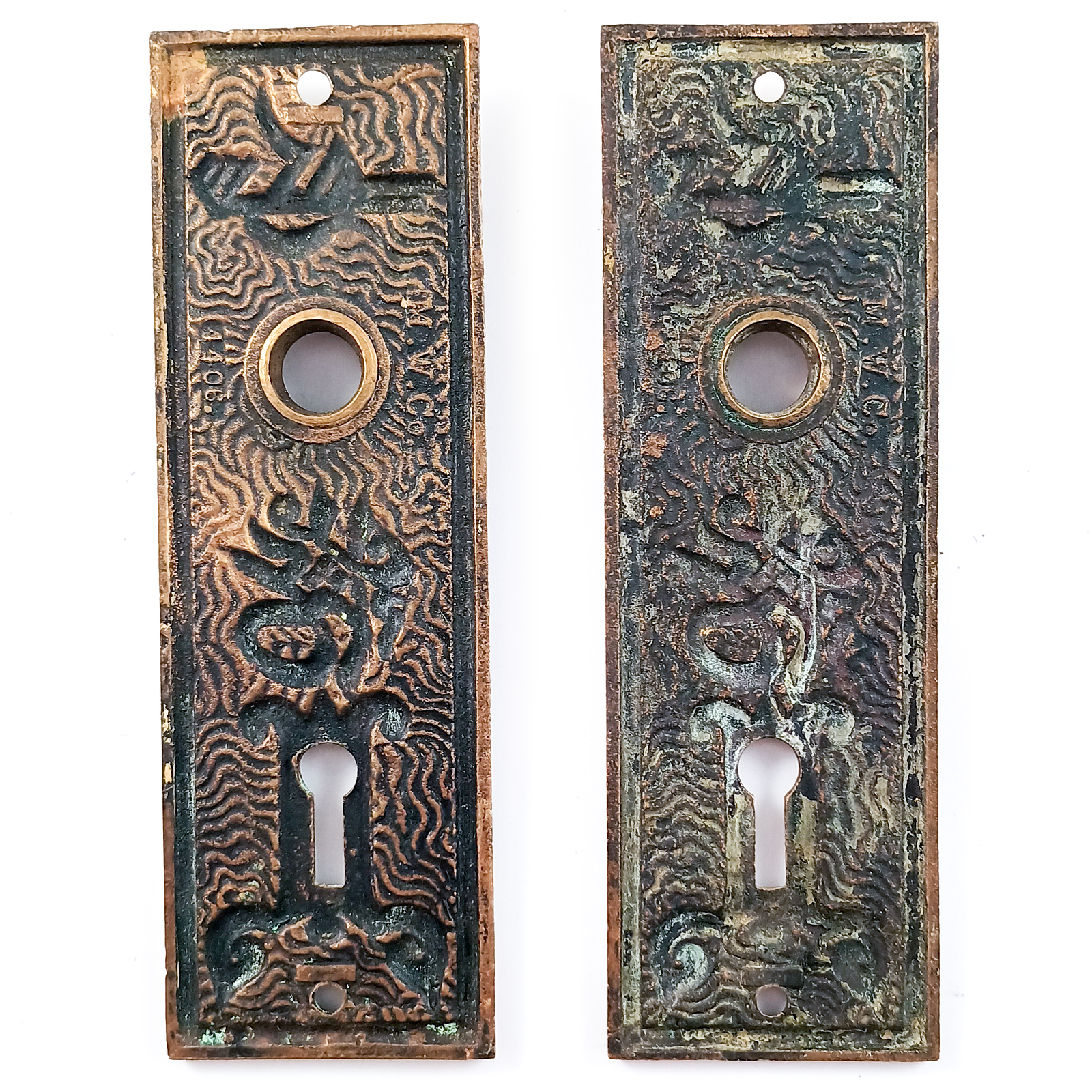 Two bronze escutcheons, each with a keyhole and a hole for a doorknob. Both escutcheons are decorated with a wavy pattern, on top of which are designs that somewhat resemble Arabic lettering and motifs