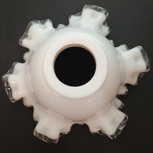 The base of a ruffled milk glass lamp shade with clear glass along the edges, photographed on a dark grey background. The fitter is unusually thick.