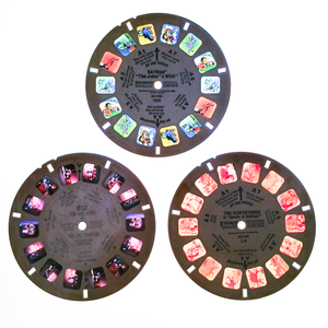 The Batman and Flintstones reels from the previous photo, as well as a Tom and Jerry reel, placed on a light box. The Flintstones reel is severely discolored, the Tom and Jerry reel looks like it may be slightly faded, and the Batman reel is in vivid color