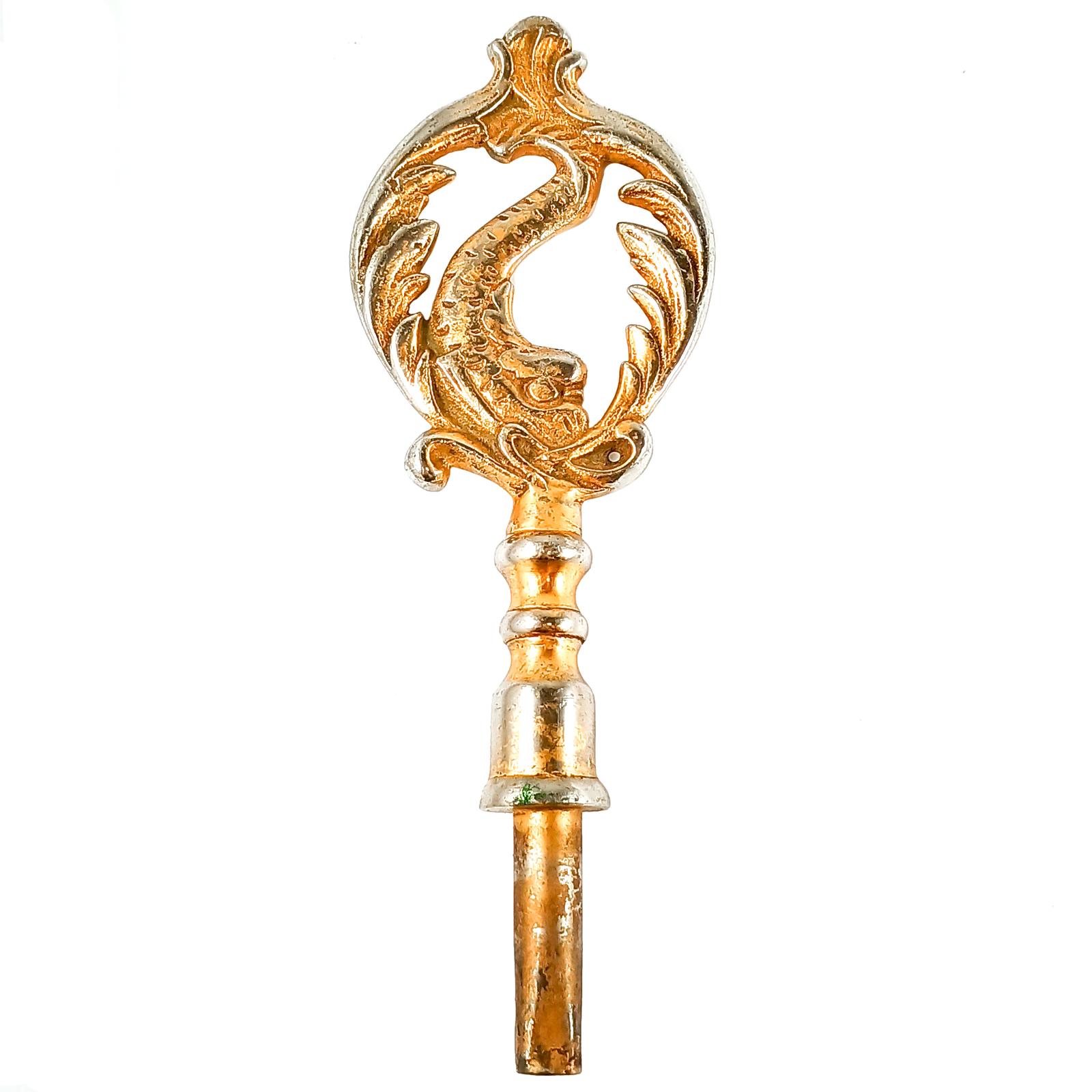 A large key consisting of a square-ended tube for the key, and a very large and ornate handle with a fish-like creature surrounded by designs shaped like cresting waves. The whole thing was originally a brassy gold tone, but you can now clearly see silver-colored metal showing through in many places.