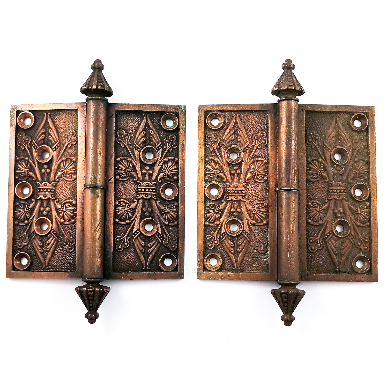 A pair of complete hinges with ornate, abstracted floral patterns on the faces. They have cone-shaped, decorate finials, and five screw holes in each face. There is significant patina on each hinge piece, and a small amount of verdigris, but the details are very well-preserved.