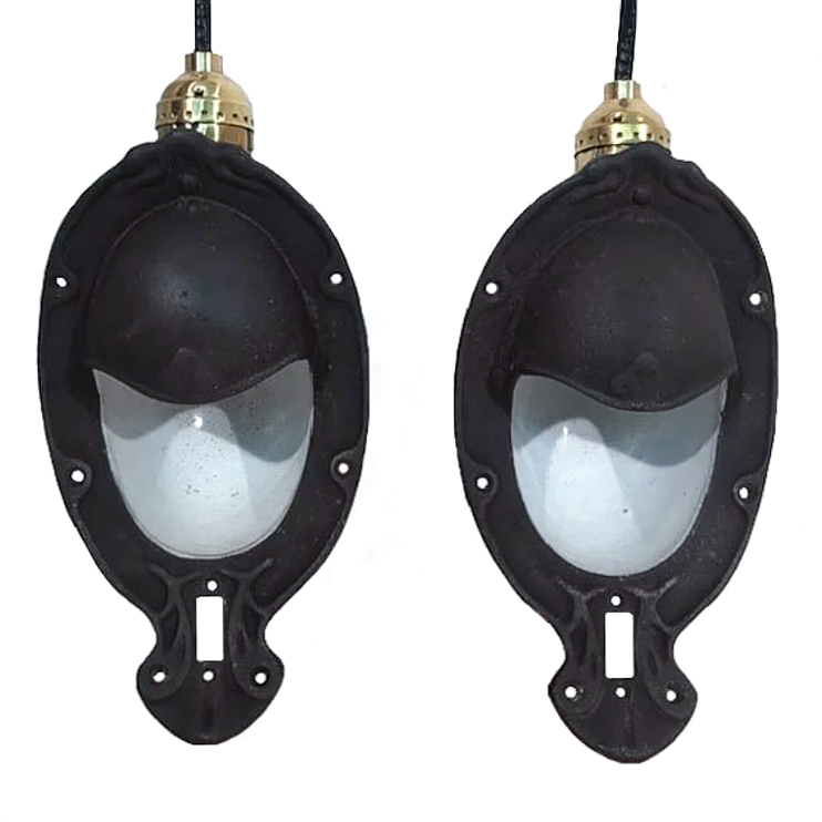 Two antique iron sconces with white enameled interiors. The sconces are oval in shape, and have a partial iron shade over where the light bulb goes.