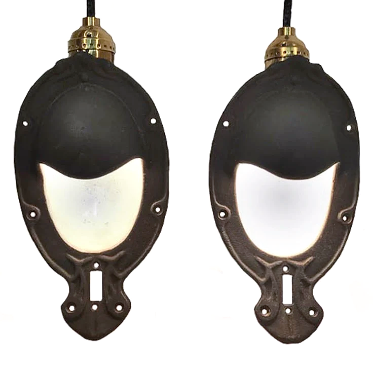 Two antique iron sconces with white enameled interiors. The sconces are oval in shape, and have a partial iron shade over where the light bulb goes.