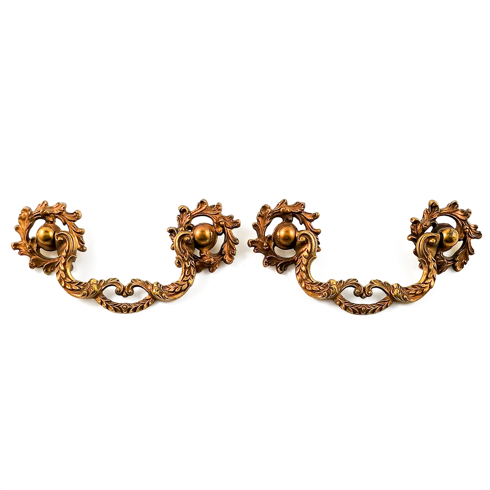 A single brass drawer handle consisting of two round mounting pieces and a handle in the middle held up by them. The mounting pieces are open acanthus leaf scroll work, and the center  piece has two curved pieces decorated with leaves, which meet in the middle and have a second curved piece below the center creating an open shape