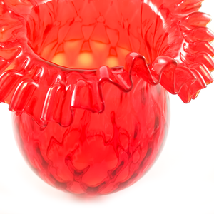 A close-up of a chip in the ruffled edge of a bright red glass lamp shade