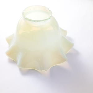 The same lamp shade upside-down, showing the translucence of the glass and the orange quality of light shining through it. There is also a thin rim of clear glass around the ruffled edges. The abase is badly chipped.