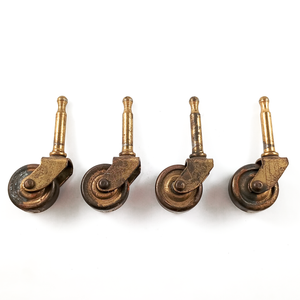 Four antique grip-neck stem casters in a line, with brass hardware and wheels. They show significant surface wear.