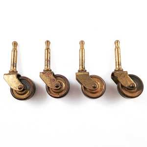 Four vintage grip-neck stem casters with brass hardware and wheels. There is a fair amount of wear visible on the surfaces.