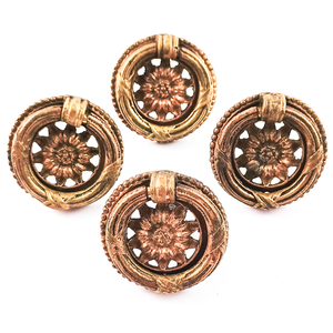 Four small brass vintage ring pulls with ornate decoration and sunflower designs in the middle.
