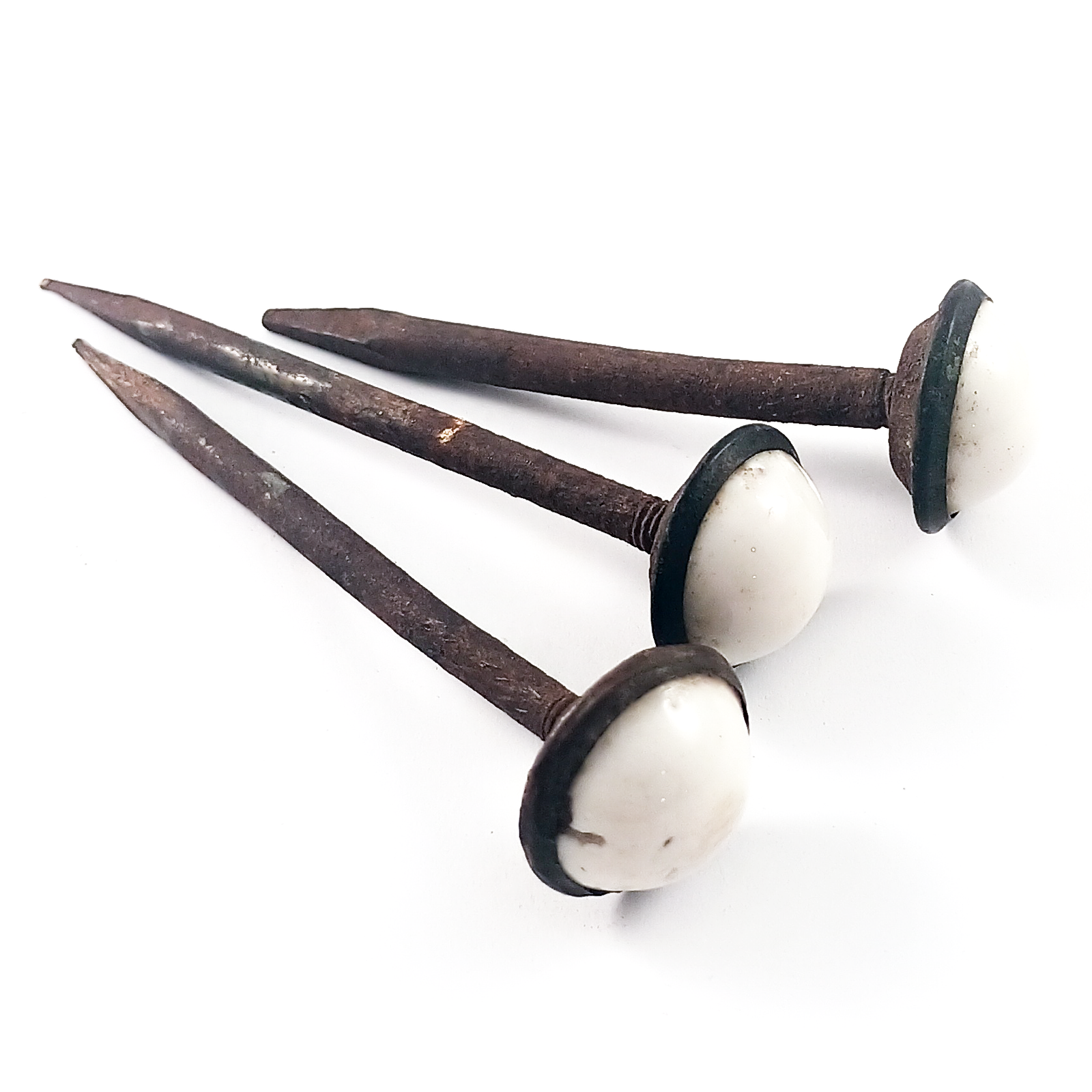 Three rusted iron nails with domed white ceramic heads in dark iron settings, showing screw threads behind the domed heads