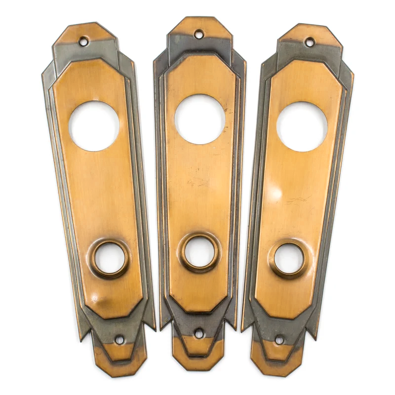 Three bronze Art Deco escutcheons with areas of dark patina and two round holes, one for a cylinder lock and one for a doorknob