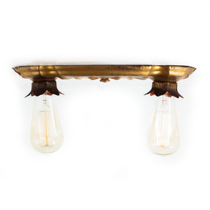 A side view of a vintage gold-tone ceiling light fixture, showing two sockets with flower-shaped housings projecting downward from the fixture, and bulbs installed in each socket.