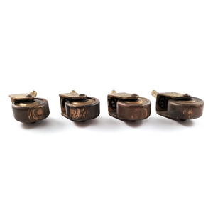 The underside of four antique brass casters, showing the surfaces of the brass wheels