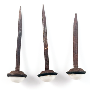 Three rusted iron nails with white ceramic heads, showing that one nail is shorter than the other two