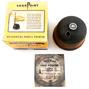 A vintage Dietzgen Sharpoint lead pointer made of cast iron with a cork grip, photographed alongside its graphite-stained original paper insert and its original yellow box