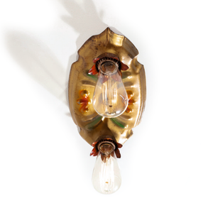 A photo of a vintage gold-tone ceiling light fixture with two sockets, each of which is housed in a red flower shape. There are red and green scrolling decorations in the middle of the fixture, and bulbs have been installed in each socket.