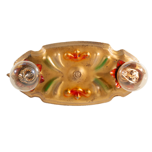 A photo of a vintage gold-tone ceiling light fixture with two sockets, each of which is housed in a red flower shape. There are red and green scrolling decorations in the middle of the fixture, and bulbs have been installed in each socket.