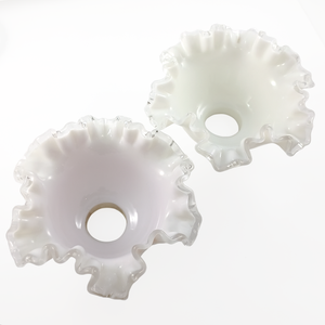 Two ruffled bell-shaped lampshades made of white glass with clear glass along the edges, photographed on a white background. One has a pinkish-purple tint.