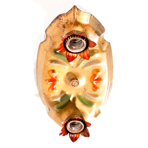 A photo of a vintage gold-tone ceiling light fixture with two sockets, each of which is housed in a red flower shape. There are red and green scrolling decorations in the middle of the fixture.