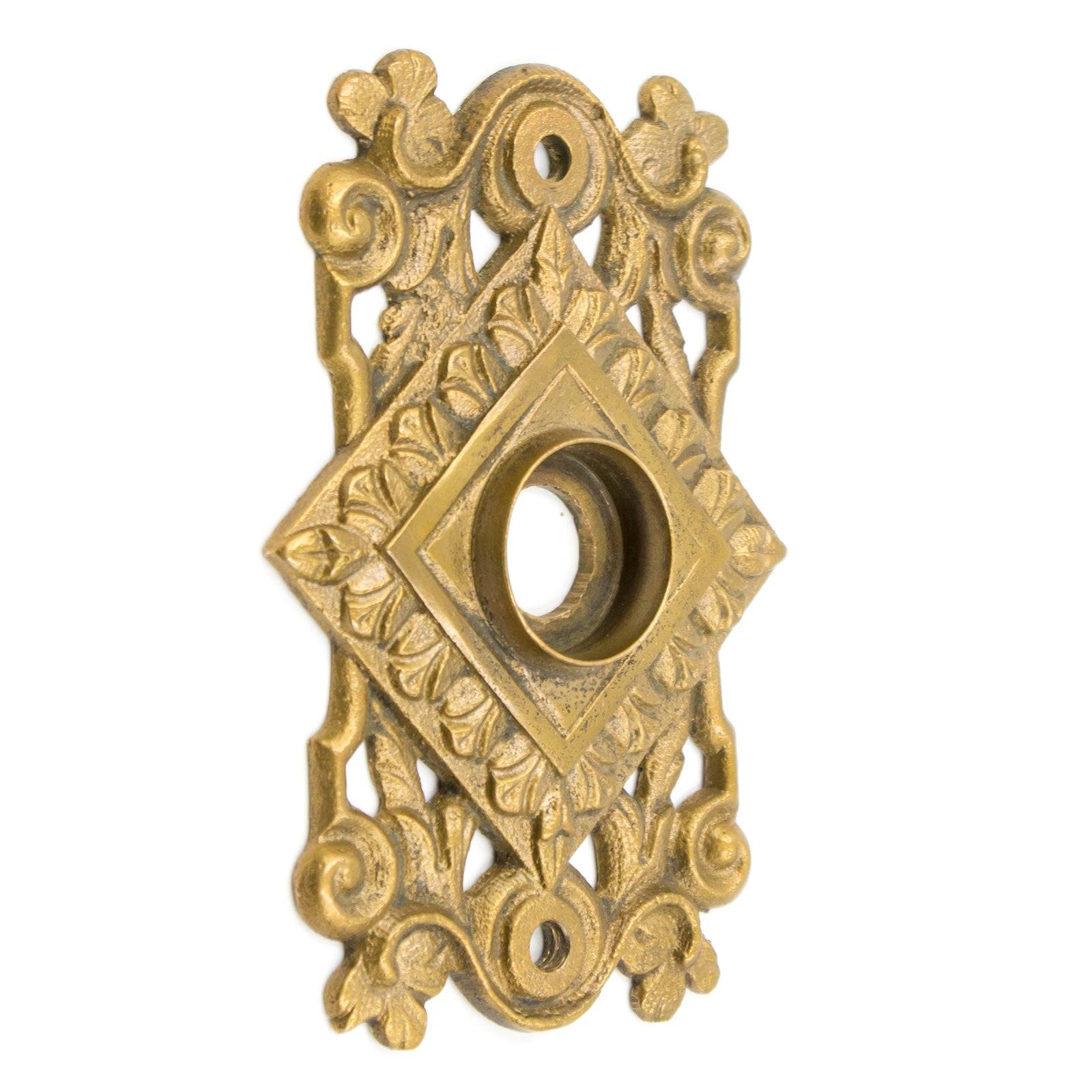 A roughly rectangular brass plate with a hole in the middle for a doorknob. There is a diamond-shaped portion in the center, which has a leafy pattern around the edge, and there are scrolling vines and leaves making up the rest of the plate.