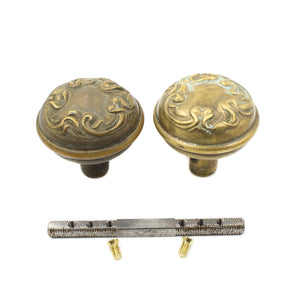 this is a picture showing a slightly angled view of a pair of two antique brass art nouveau doorknobs and a spindle and set screws 