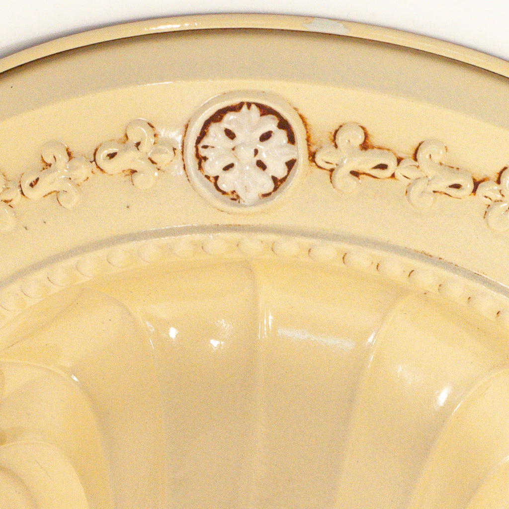 this picture shows the floral detail on the canopy of a vintage bare bulb ceiling fixture. The floral detail in this picture is butter yellow