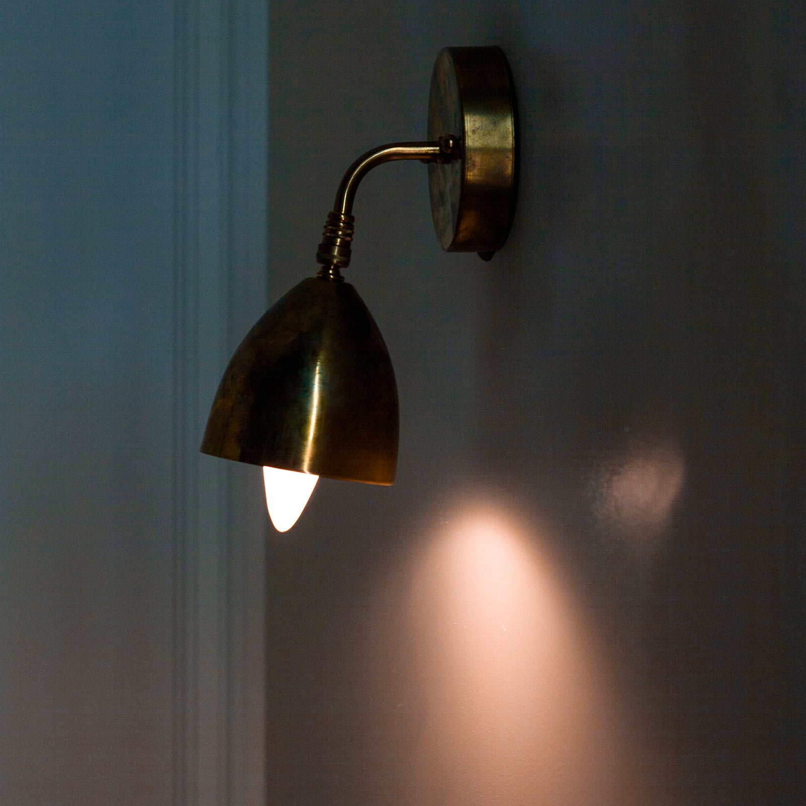 A vintage brass wall sconce shown from the side, with a bell-shaped shade and a bulb installed for display